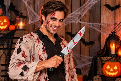 Mann mit Halloweenkostüm und blutigem Horror-Spielzeugmesser in einer Halloween-Kulisse