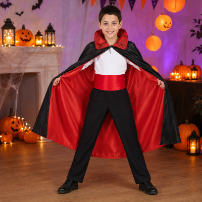 Kind mit schwarz-rotem Vampir-Umhang, Schärpe und Spinnennetz-Kragen in einer Halloween-Kulisse